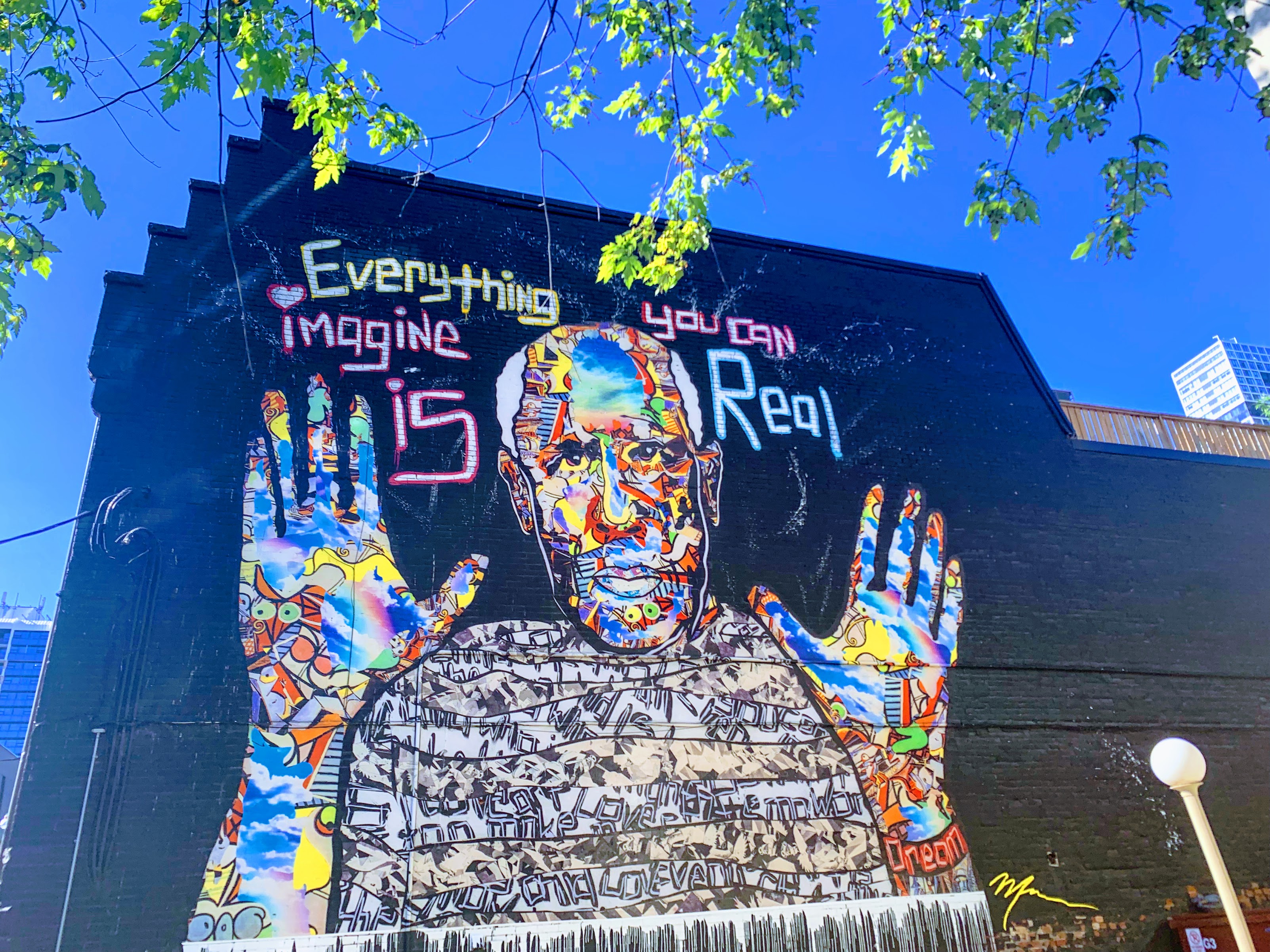 A colourful mural on a brick wall beneath a blue sky, with the words “Everything you can imagine is real.”